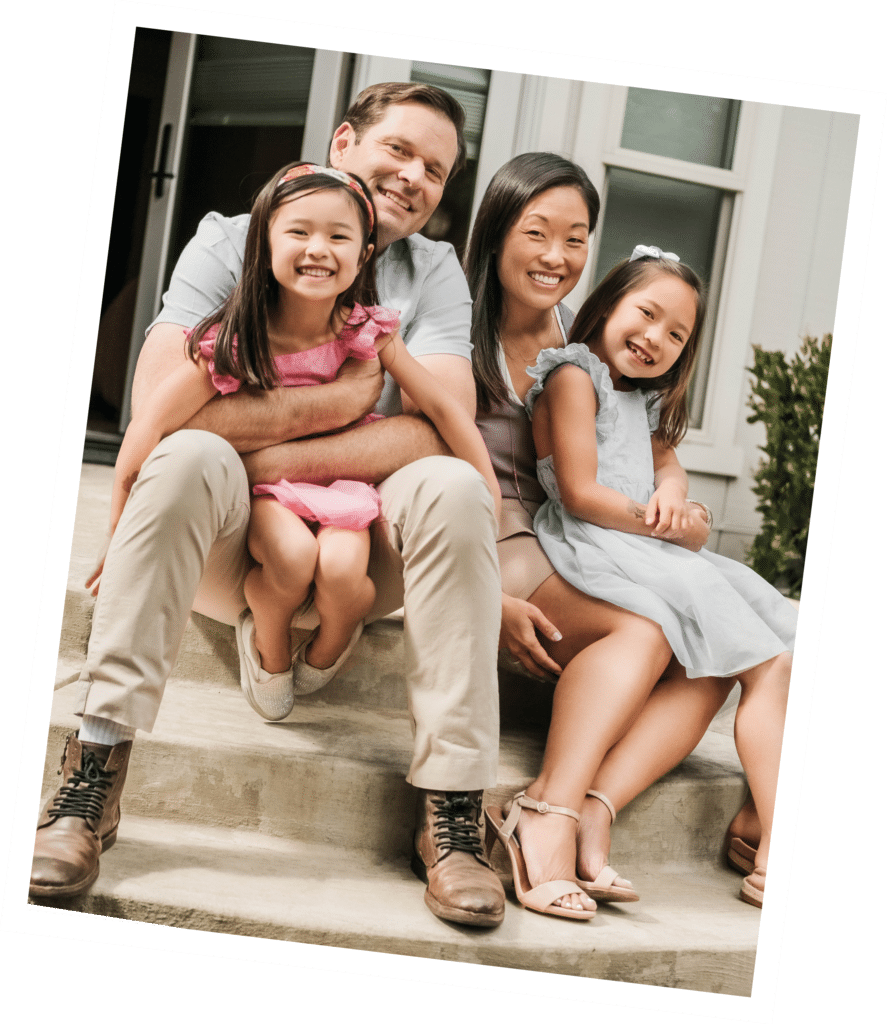 Smiling family seated on steps in front of a house, two adults and two children.