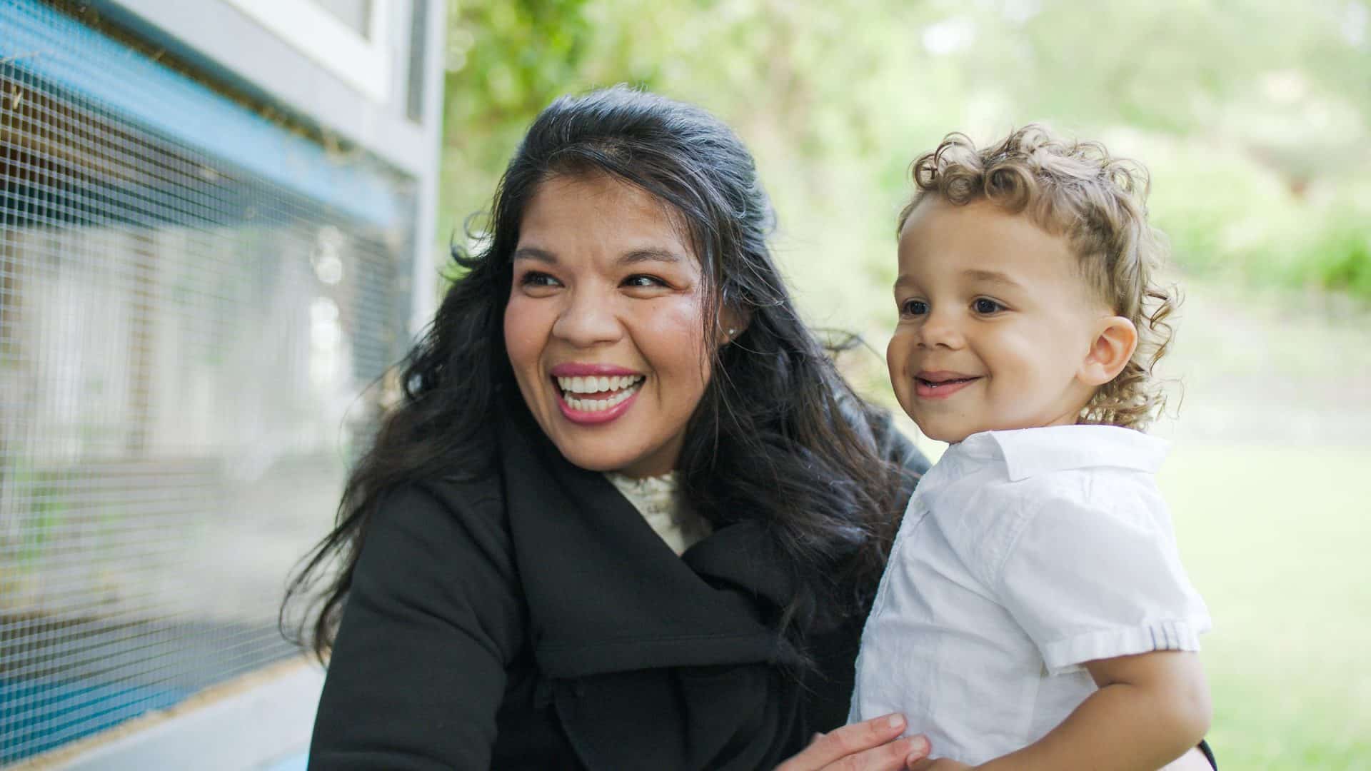 A smiling woman and child gaze at something outside, standing near a window, a familiar scene supported by the loving touch of an Idaho Nanny Agency caregiver.