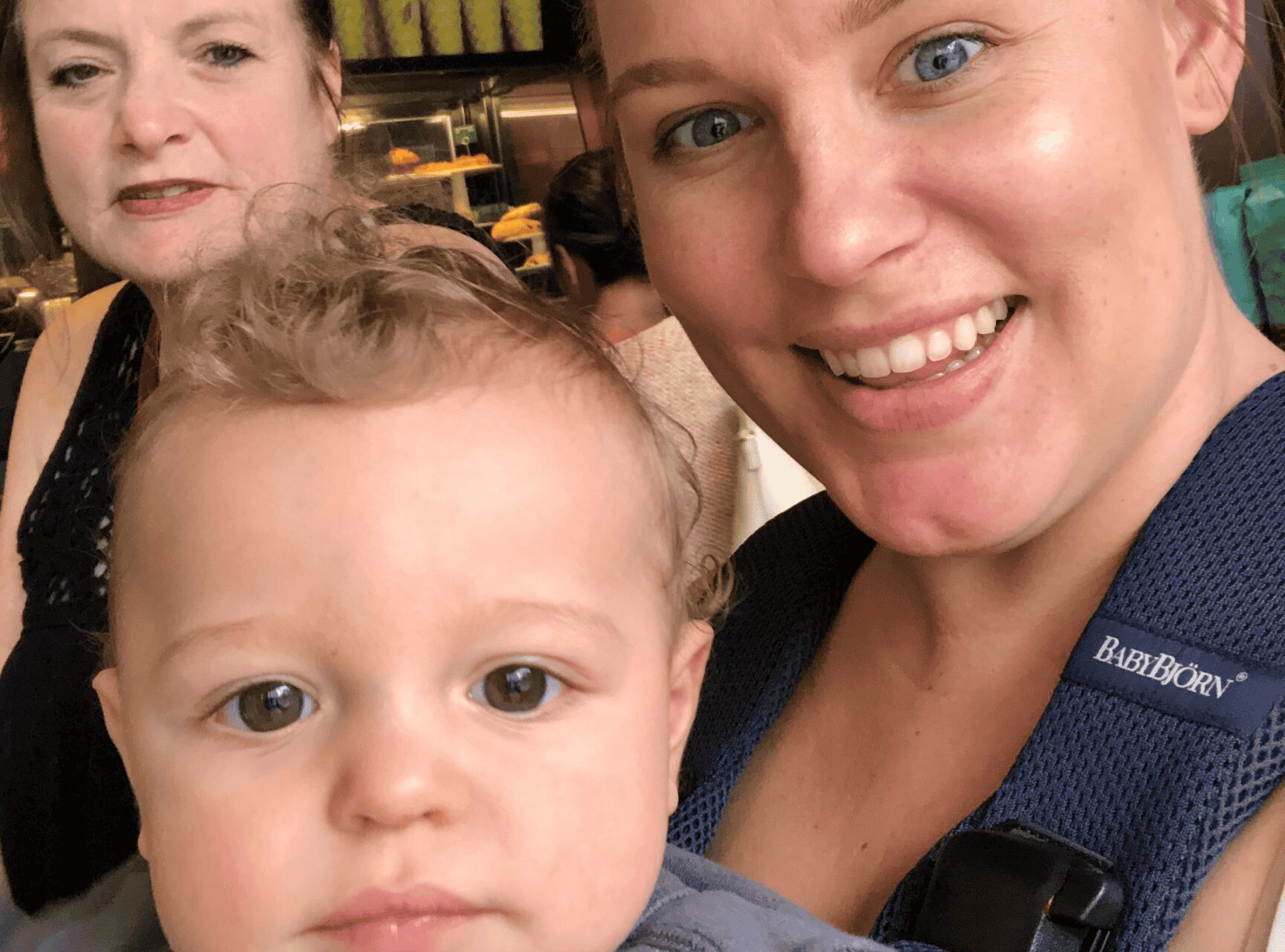 Two women and a baby, wrapped snugly in a carrier worn by one of the women, smile warmly at the camera. Their joy is as clear as the investment of love they share, highlighting life's most genuine ROI.