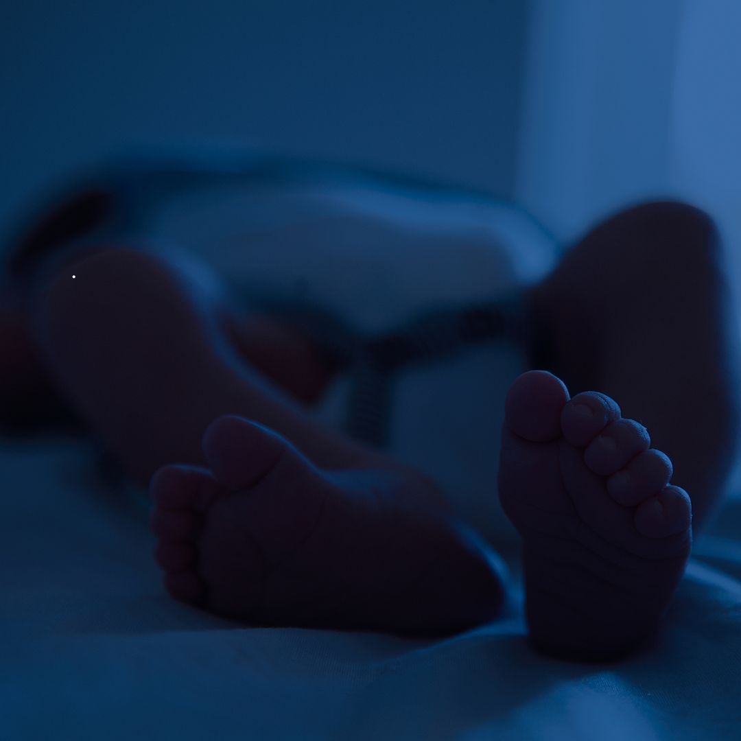 A baby peacefully sleeping in a crib, tiny feet tucked under a blanket, with a soft blue light casting a gentle glow—a serene moment in the early stages of infant sleep training.