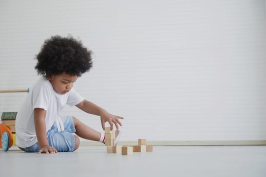 Child sitting on the floor, playing with wooden blocks in a bright, minimalist room.