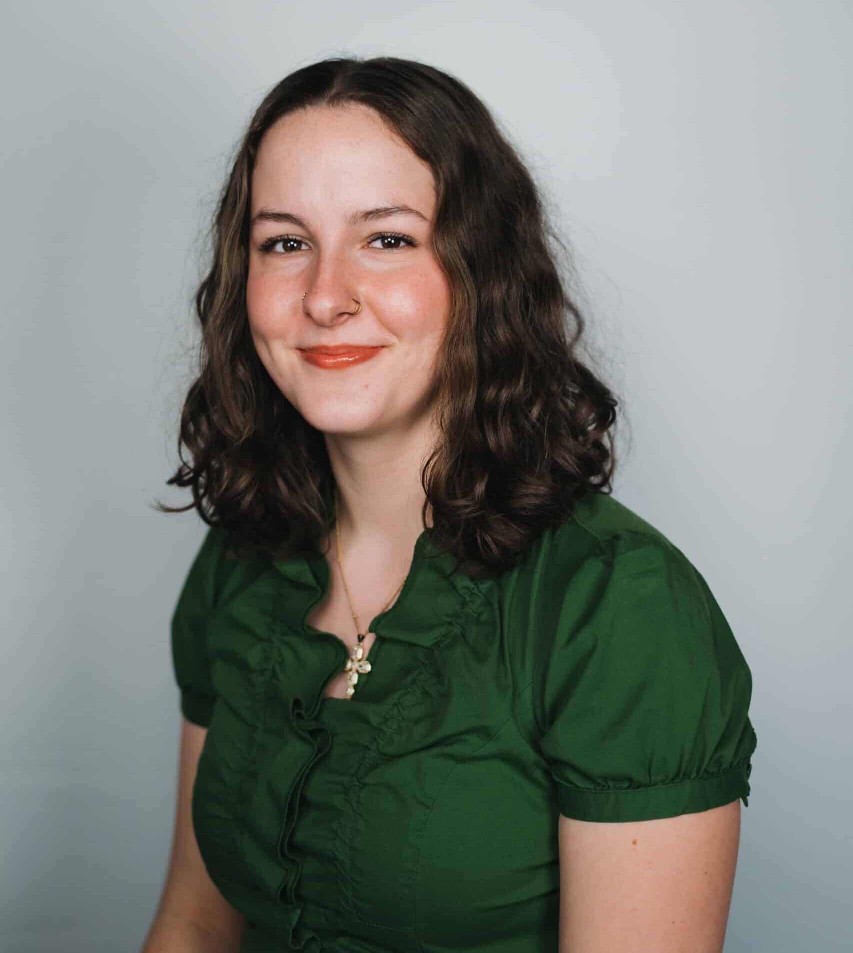 Person in a green blouse smiling against a neutral background.