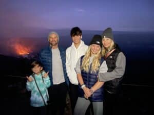 A family of five poses outdoors at dusk with a glowing volcano in the background, reminiscent of scenes discussed in the recent Keesha Scott interview.