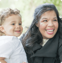 Smiling woman in a black coat holding a happy young child outdoors.