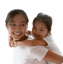 Smiling woman giving a piggyback ride to a happy young child, both wearing white shirts.