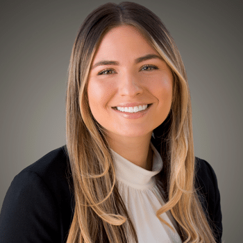 A woman with long, straight hair smiles in a professional headshot against a gray background.