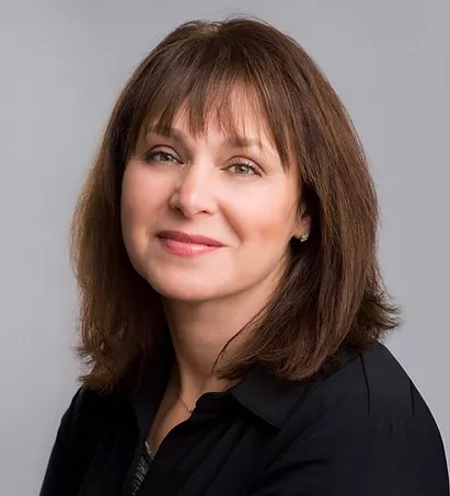 Woman with shoulder-length brown hair wearing a black top, smiling softly against a gray background.