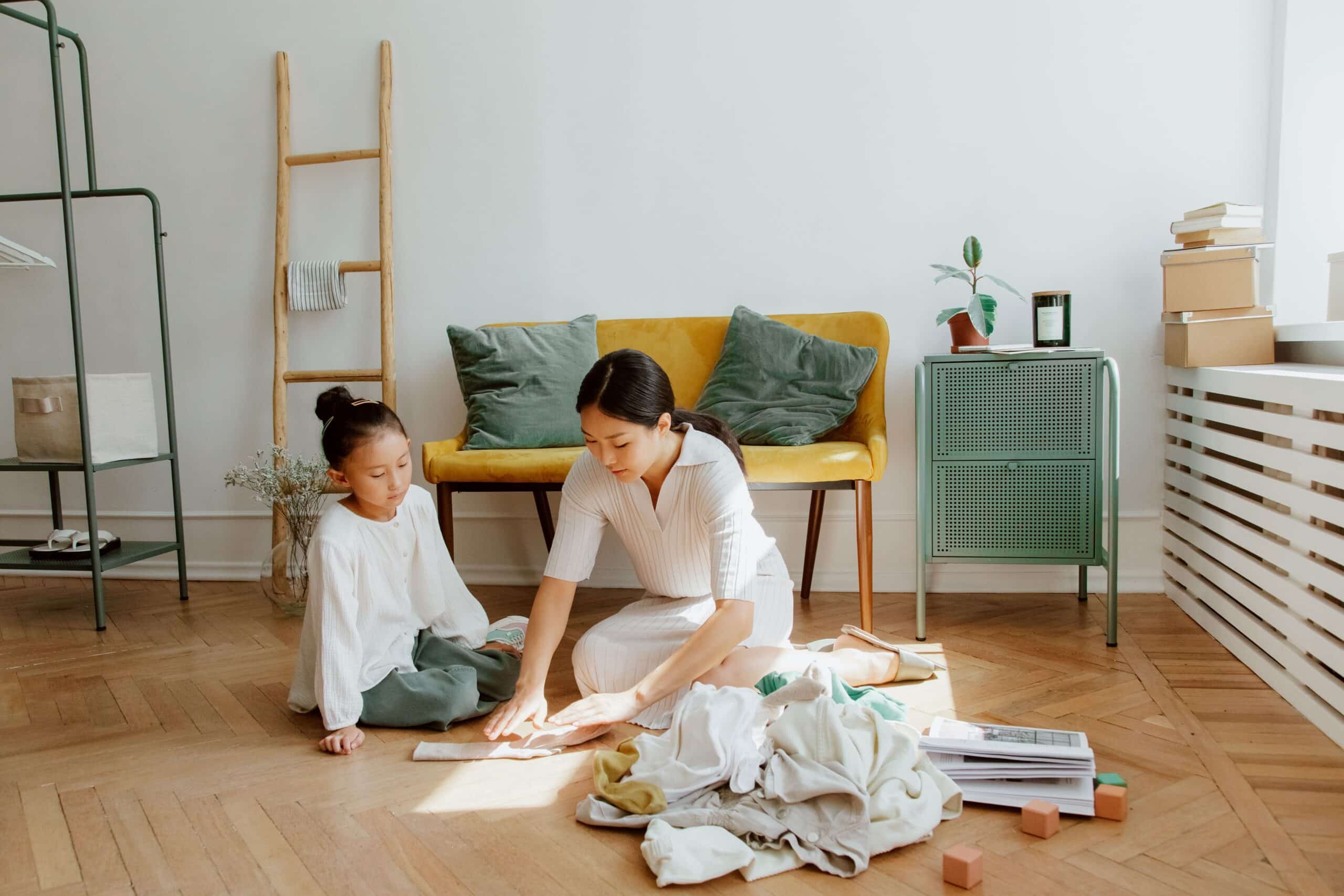 A woman and a young girl sit on the floor, folding laundry together in a bright, cozy living room as part of their Sunday Reset.